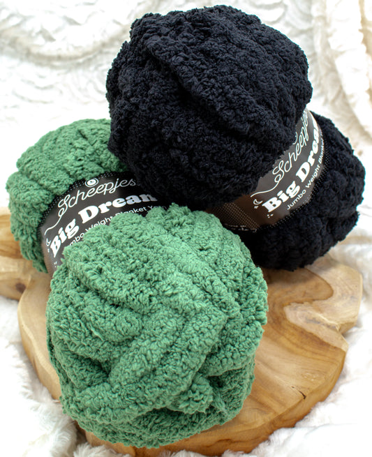 Twee bollen Scheepjes Big Dreams garen, in groen en zwart, op een houten ondergrond