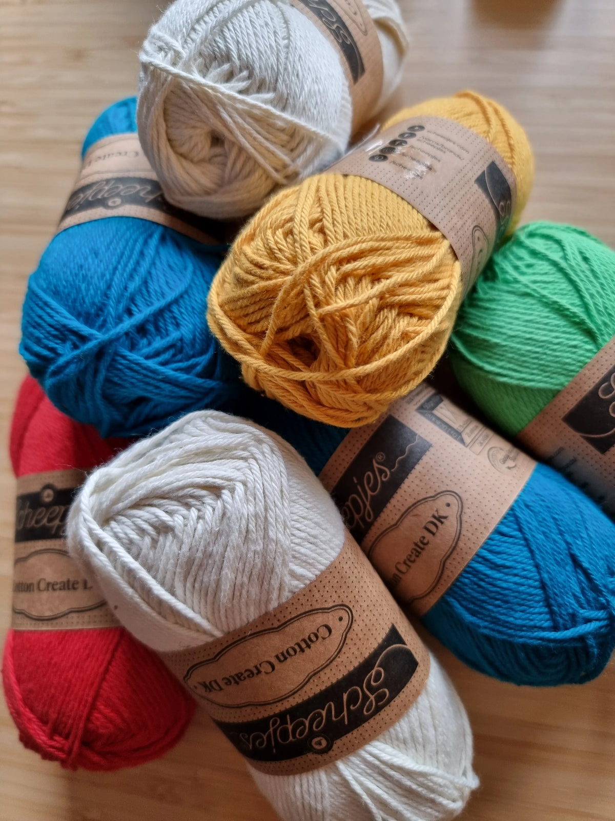 Verschillende kleuren Scheepjes Cotton Create DK bij elkaar op een houten ondergrond