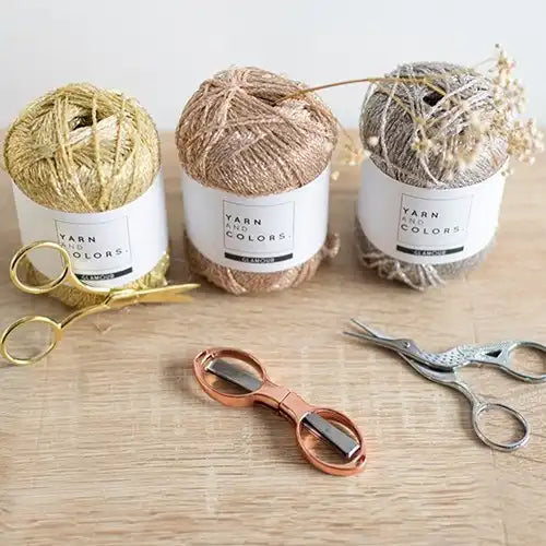 Drie bollen Yarn and Colors Glamour naast elkaar, goud, rose goud en zilver, met schaartjes erbij