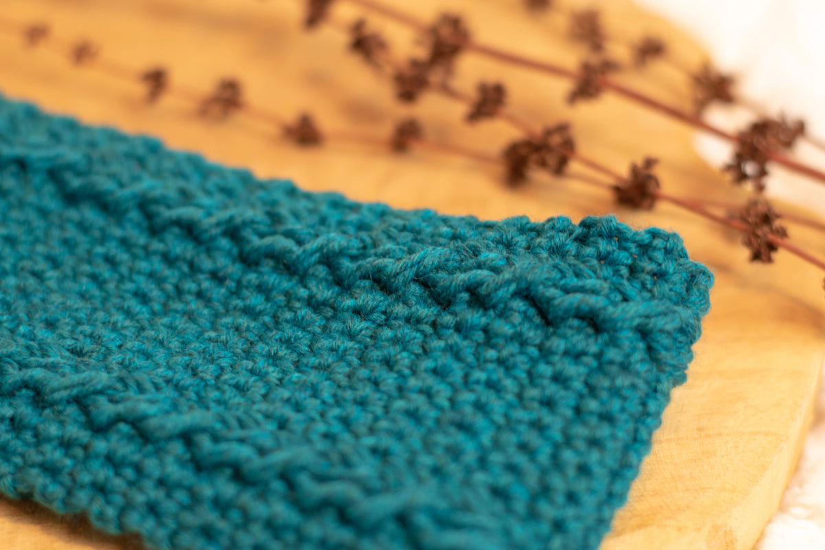 Close up van blauwe gehaakte hoofdband gemaakt met Haakpatroon hoofdband Merel ontworpen door Cora's Knit Knacks