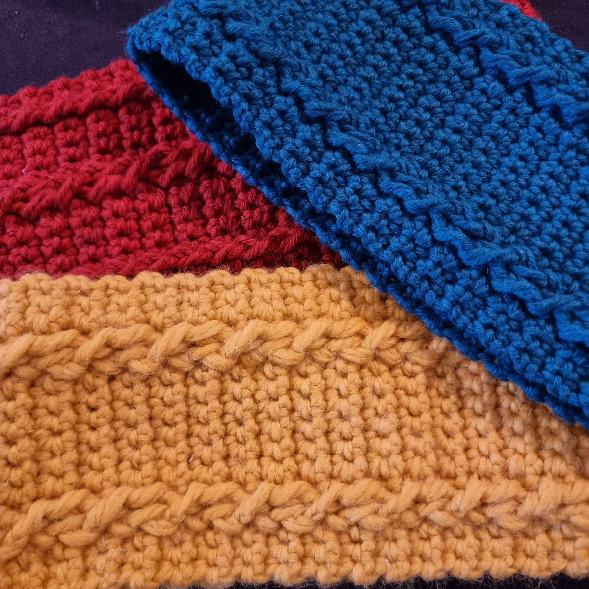 Drie verschillende gehaakte hoofdbanden over elkaar, een rode hoofdband Koekoek en een gele en blauwe hoofdband Merel, alle drie ontworpen door Cora's Knit Knacks, gemaakt met haakpatroon hoofdband Koekoek en haakpatroon hoofdband Merel