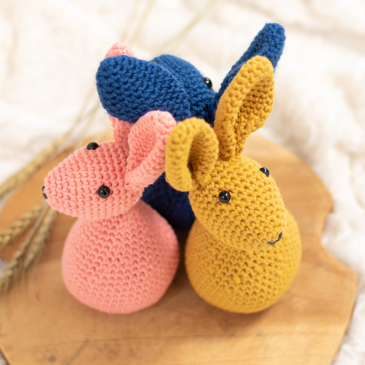 Drie gehaakte konijnen Sem, in okergeel, licht oranje en donkerblauw bij elkaar voor haakpatroon konijn Sem ontworpen door Cora's Knit Knacks