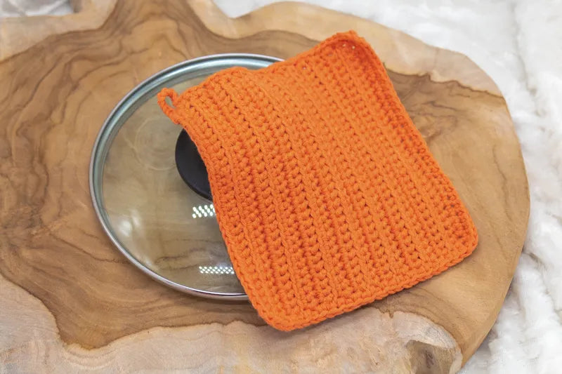 Oranje gehaakte pannenlap op een pannendeksel gemaakt met Haakpatroon pannenlap Ridge ontworpen door Cora's Knit Knacks