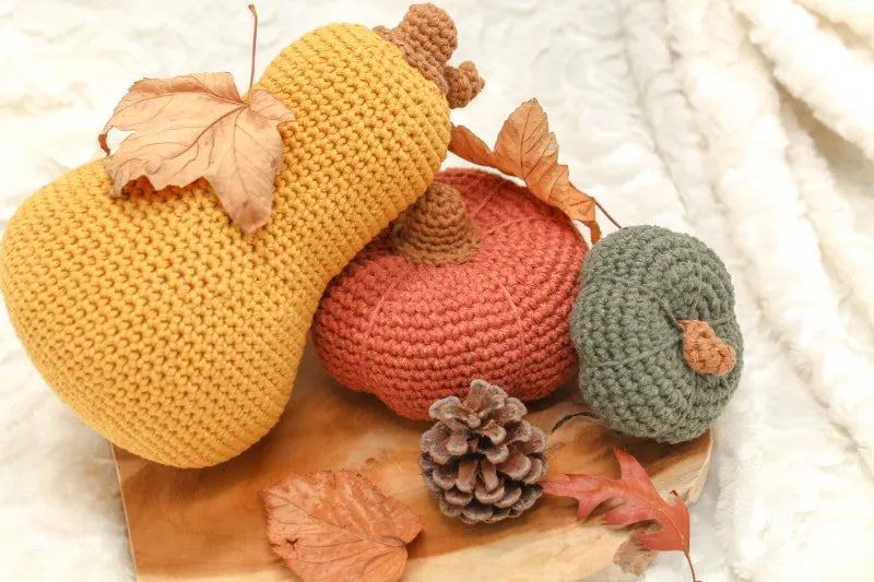 Donkergroene gehaakte kleine pompoen gemaakt met haakpatroon pompoen Kaddu, samen met donkeroranje gehaakte pompoen gemaakt met haakpatroon pompoen Zucca en okergele gehaakte flespompoen gehaakt met haakpatroon flespompoen Finn, alle drie ontworpen door Cora's Knit Knacks