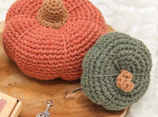 Donkergroene gehaakte pompoen gemaakt met haakpatroon pompoen Kaddu, samen met donkeroranje gehaakte pompoen gemaakt met haakpatroon pompoen Zucca, beide ontworpen door Cora's Knit Knacks