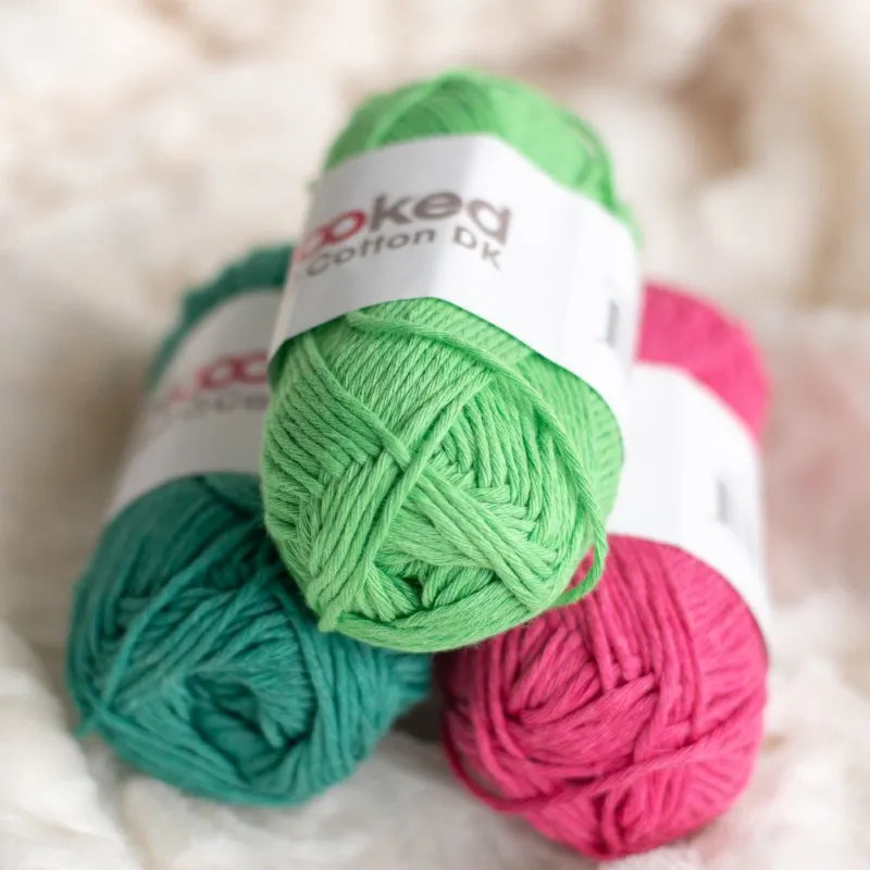 Drie bolletjes Hoooked Soft Cotton DK liggen op een witte deken, bolletjes in de kleuren groen, donkergroen en fel roze