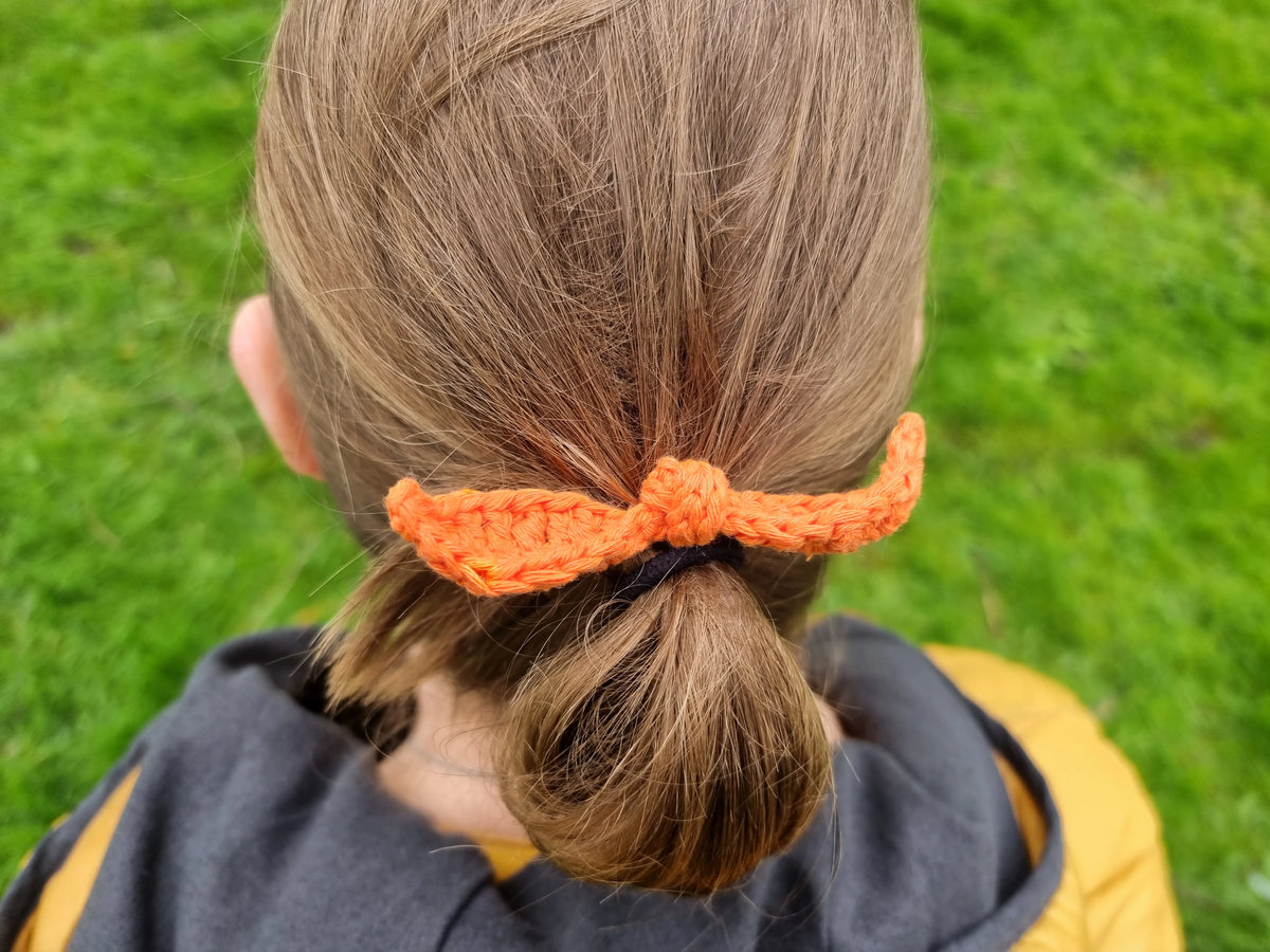 Gehaakt Haakpatroon strikje Sisi ontworpen door Cora's Knit Knacks, oranje gehaakt strikje in het haar van een vrouw