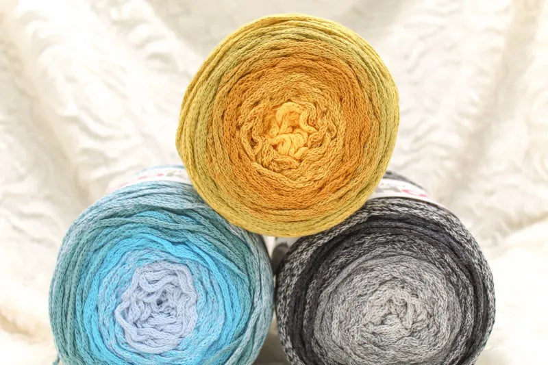 Drie bollen Hoooked Wavy Blends die op elkaar liggen: blauwtinten, zwarttinten en geeltinten