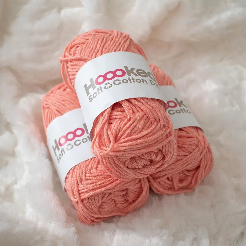 Drie bolletjes Hoooked Soft Cotton DK in licht oranje liggen op een witte deken